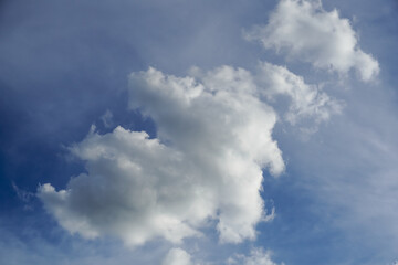 Fluffy white cumulus clouds drift across a clear blue sky on a bright day © Thanakrit