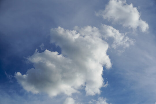 Fluffy white cumulus clouds drift across a clear blue sky on a bright day