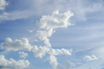 Fluffy white cumulus clouds drift across a bright blue sky on a sunny day © Thanakrit