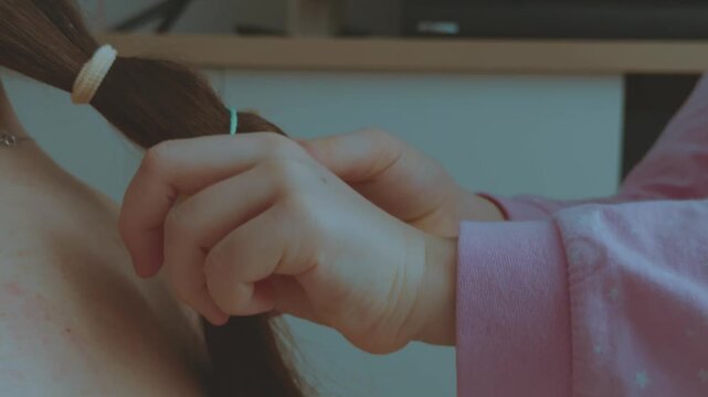 A girl braids her mother's hair, a daughter braids her hair, a child braids her hair