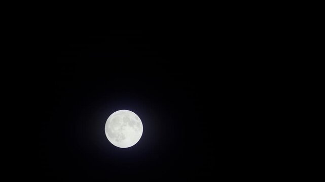Full moon glowing with soft blue halo against pure black night sky, surface craters and texture clearly visible in close-up telephoto shot