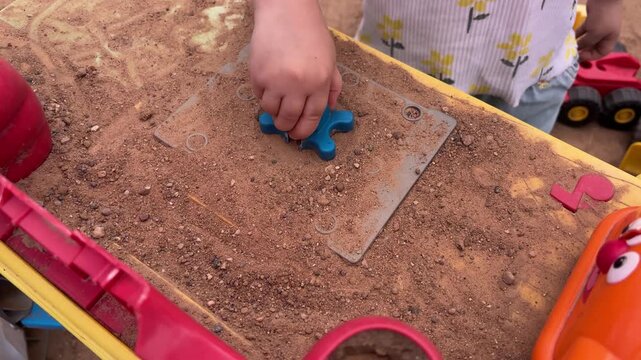 Child hand playing with a blue plastic toy in a sandbox with small stones