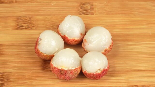 Macro shot of human hands arranging fresh peeled red lychee fruits on a wooden cutting board