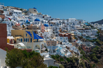 Sunlit Cycladic houses and churches cascading down a cliff above the Aegean Sea on Santorini, Greece. © Andrei Tomas
