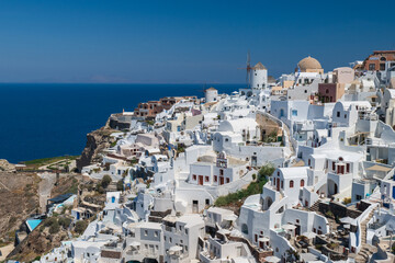 Panoramic view of whitewashed houses and windmill on Santorini caldera above deep blue water on a sunny summer day. © Andrei Tomas