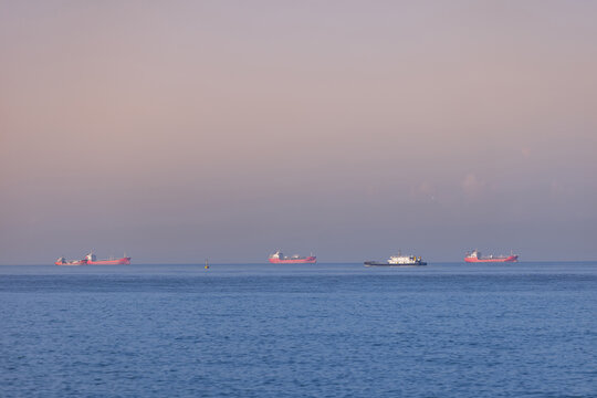 Cargo ships anchored waiting on calm sea at dusk horizon
