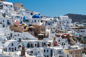 Sunlit Cycladic architecture on Santorini hillside, Greece, with white buildings and blue church domes under clear summer sky. © Andrei Tomas