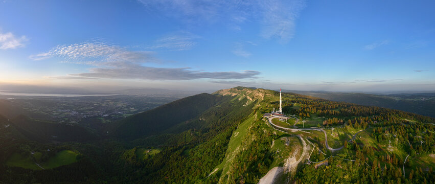 Aerial view of Col de la Faucille featuring a communication tower atop lush green mountain slopes, dense forests, and a panoramic view of the valley in Gex, Auvergne-Rhone-Alpes, France.