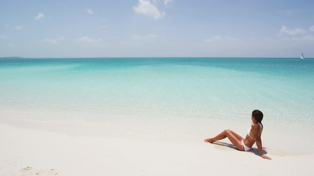 Beach woman sunbathing relaxing at perfect paradise beach on travel vacation looking enjoying view of ocean. Relaxed woman in bikini lying down on beach on summer holidays. Luxury island resort hotel.