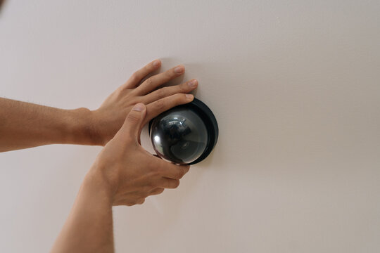 Close-up view of male hands installing black dome surveillance camera on white ceiling. Concept of home security, protection, monitoring, smart home technology installation.