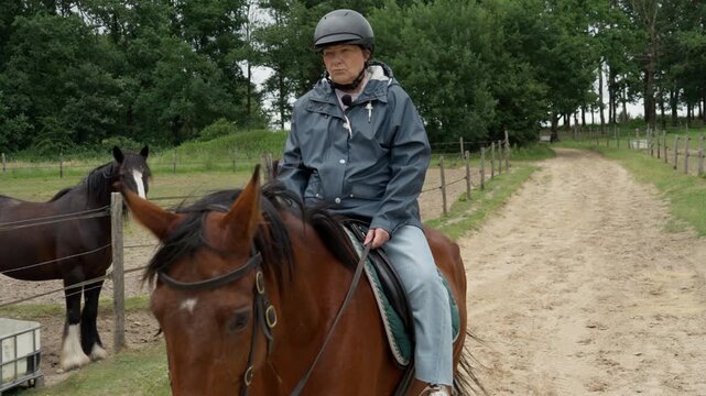 Active senior woman enjoys equestrian tourism riding horse on rural farm pathway. Elderly citizen experiences outdoor recreation, healthy longevity lifestyle, and countryside holiday hobby travel.