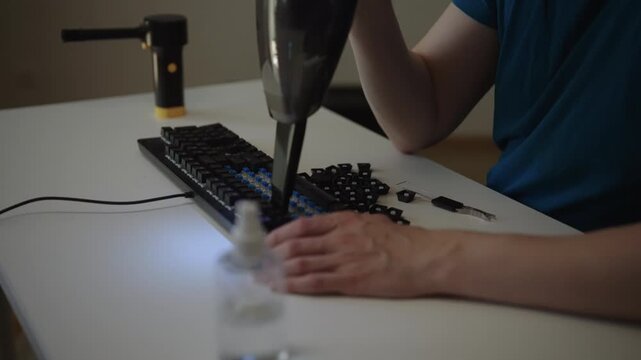 Detail professional person using handheld vacuum cleaner to remove dust from disassembled mechanical keyboard, demonstrating meticulous electronic device maintenance and computer hardware care