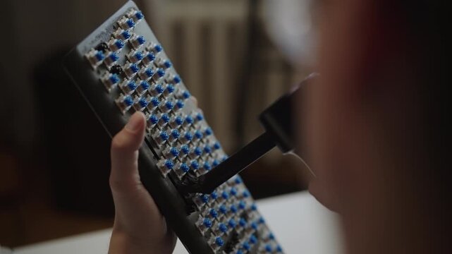 Close-up over shoulder shot of technician using rubber air blower to clean dust from blue switches of custom mechanical keyboard during routine maintenance service. Shooting in slow motion