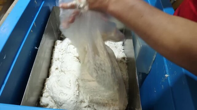 Close-up of a worker mixing and preparing thick white dough for traditional Korean fish cakes inside a metal machine at a food production factory.
