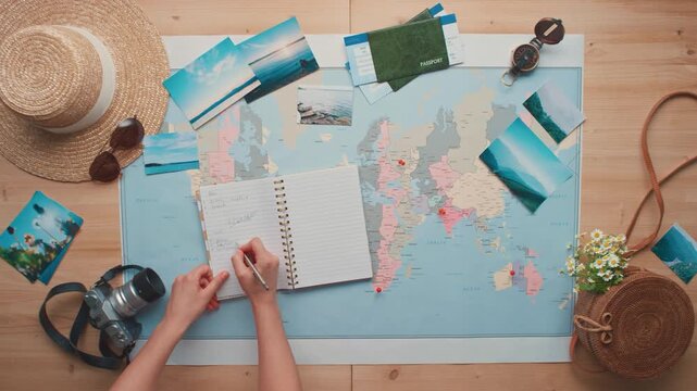 Top view of a person planning a summer vacation trip on a world map with travel accessories and photographs