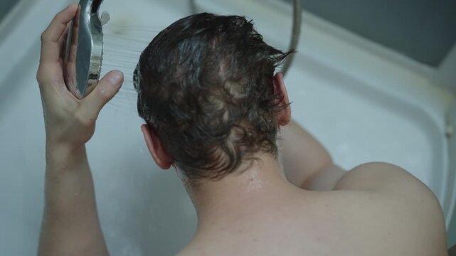 Top down view of man rinsing shampoo from dark, wet hair using shower head. daily hygiene routine includes showering and conditioning for personal care and cleanliness
