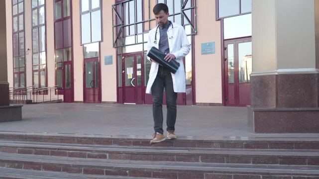 Doctor wearing lab coat stethoscope analyzing X-ray image outdoors stand near hospital main entrance. Young healthcare professional, internet radiologist exam mri x-ray lungs during COVID 19 epidemic.