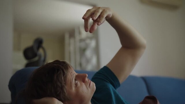 Troubled adult man lying on sofa at home, thinking and touching hair experiencing anxiety, stress, depression, loneliness in living room during daytime. Shooting in slow motion