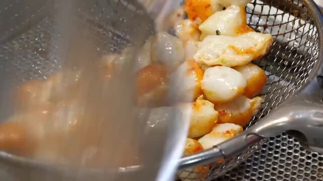 A close up shot of golden brown fried Korean fish cakes, also known as eomuk or odeng, sitting freshly cooked in a metal wire mesh strainer at a street food market.