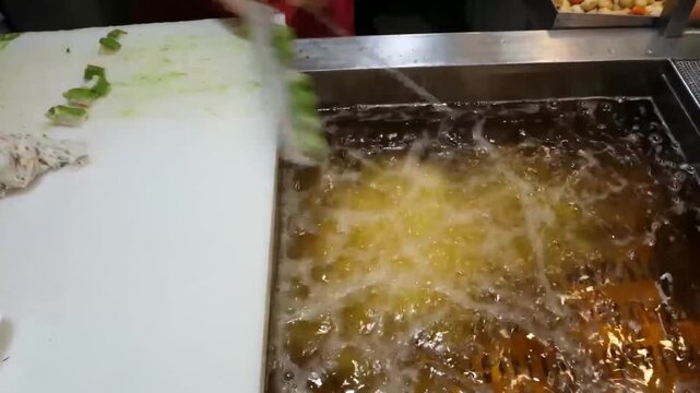 close-up shot of a street food vendor expertly deep-frying handmade Korean fish cakes (Eomuk) in hot oil. The video captures the authentic process of shaping and frying the savory fish paste until gol