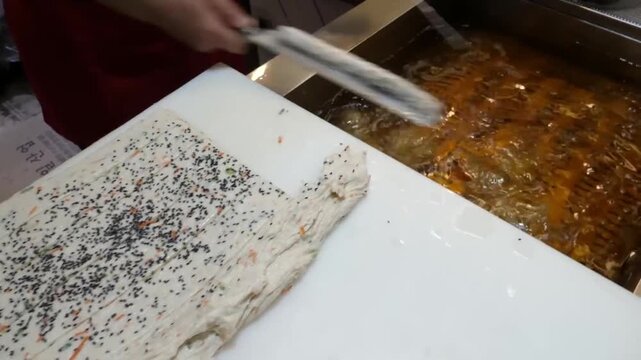 Close-up footage of the traditional process of making Korean fish cakes, also known as Eomuk or Odeng. A vendor is seen spreading fresh fish paste mixed with carrots and black sesame seeds on a board 