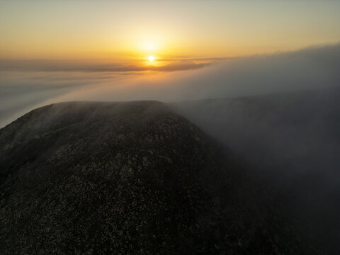 Aerial view of a mountain peak rising above a thick layer of clouds during a golden sunset in El Cotillo, Canary Islands, Spain.
