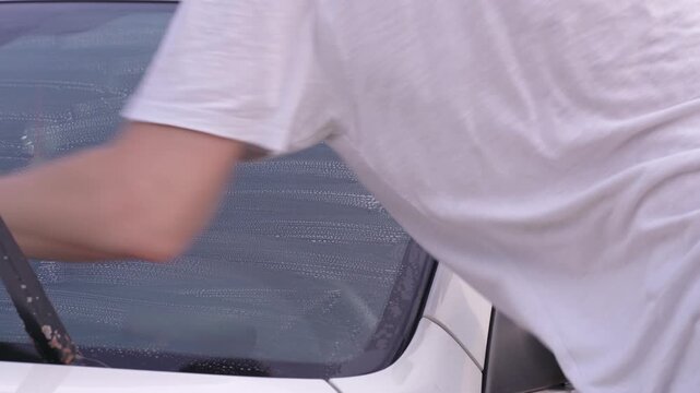 A man washes car windows with detergent before applying anti-rain