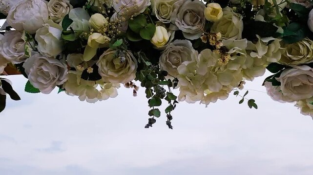 Beautiful Wedding Flower Decoration Featuring White Roses and Hydrangeas Hanging from an Arch Against a Bright Overcast Sky