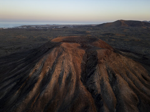 Aerial view of the Calderon Hondo volcano crater with rugged volcanic slopes illuminated by sunset light in the arid landscape of La Oliva, Canary Islands, Spain.