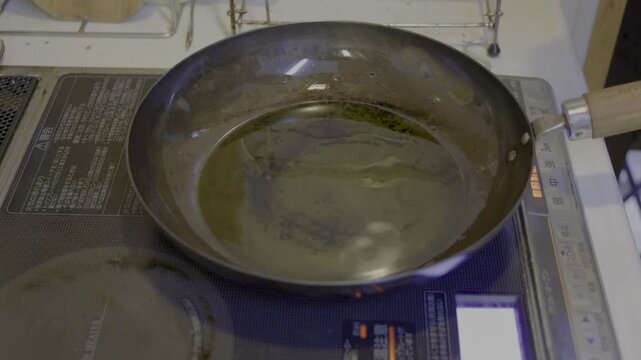 鉄フライパンにオリーブオイルを入れ、さらに鰤のアラを投入し、焼き霜するシーン
