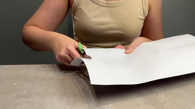Person trimming large white sheet with green scissors during tabletop craft preparation