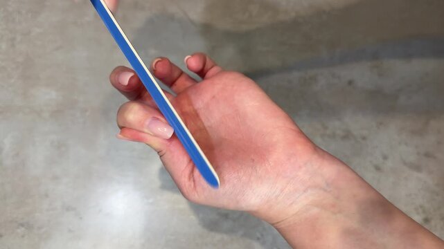 Closeup midsequence hand filing fingernail with blue emery board centered right over neutral