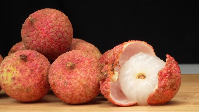 Macro close up of an opened lychee fruit showing white juicy pulp next to whole fruits