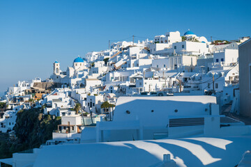 Sunlit Cycladic architecture with blue domes on Santorini’s caldera ridge under a clear sky. © Andrei Tomas