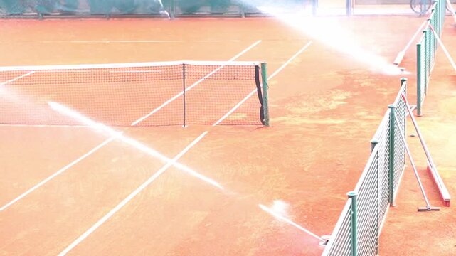Sprinkler system watering empty clay tennis court before match, sport facility maintenance video
