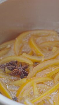 Candied orange peel simmers in bubbling syrup with star anise inside a saucepan. Concept of homemade citrus candy and dessert recipe