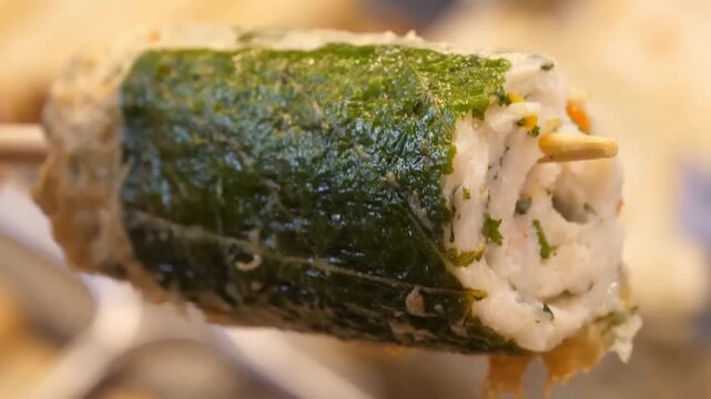 Close up footage of a freshly fried Korean handmade fish cake bar wrapped in a green perilla leaf on a wooden stick at a traditional street food market.