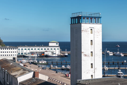 View of the control tower at the end of the pier in Sassnitz, Mecklenburg-Vorpommern, Germany, with Baltic Sea water, harbor entrance, and coastal town in the background.
