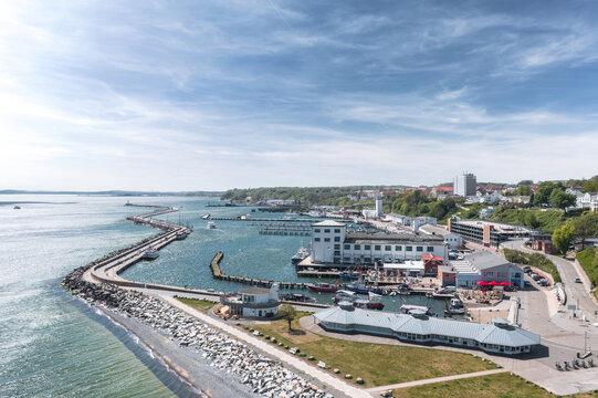 Aerial view of harbor facilities and waterfront in Sassnitz, Mecklenburg-Vorpommern, Germany, with Baltic coast, industrial port structures, and town buildings under clear daylight.