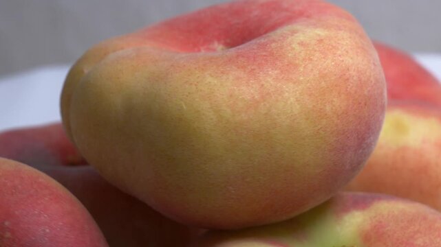 Close-up of a pile of flat donut peaches rotating on a white turntable, showcasing their unique shape and fuzzy skin under bright studio lighting.