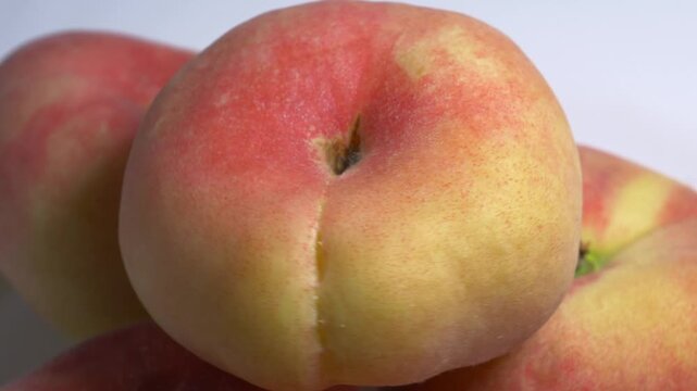 Close-up of a pile of flat donut peaches rotating on a white turntable, showcasing their unique shape and fuzzy skin under bright studio lighting.