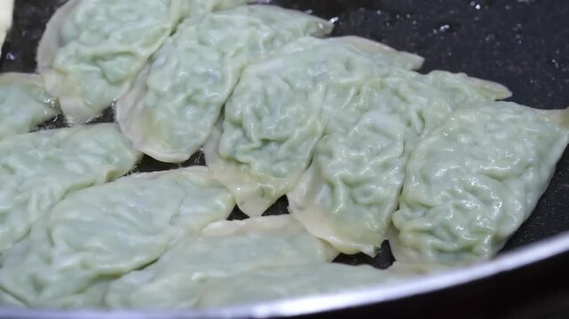 A high-angle, close-up shot of popular South Korean street snacks cooking on a seasoned flat-top grill. On one side are Napjak-mandu, a specialty of Daegu characterized by their thin, flat shape and m