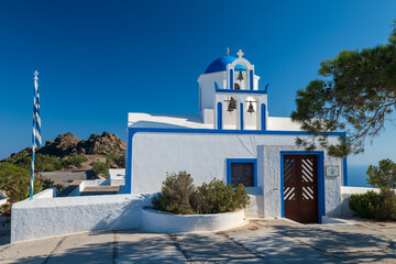 Whitewashed chapel with blue dome, cross, and bell tower under clear summer sky in Santorini, Greece. © Andrei Tomas