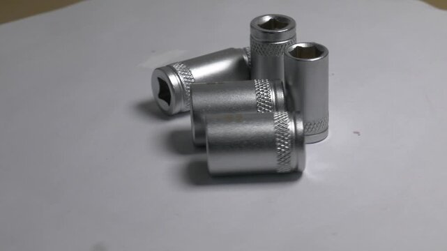 Close-up of metal socket wrench bits rotating on a white turntable, highlighting their metallic texture and knurled details under bright studio lighting.