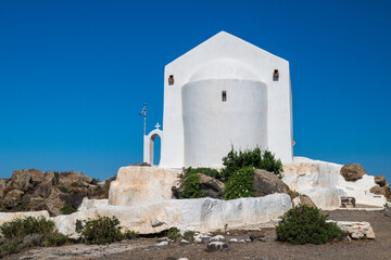 Minimal whitewashed church on volcanic rocks under clear blue sky, Santorini, Greece. © Andrei Tomas