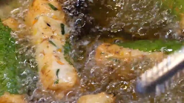 Extreme close up footage of traditional Korean fish cake bars wrapped in fresh perilla leaves deep frying in sizzling hot boiling oil with bubbles.
