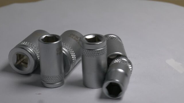 Close-up of metal socket wrench bits rotating on a white turntable, highlighting their metallic texture and knurled details under bright studio lighting.