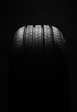 Car tire on dark background, front view. Moody automotive concept shot highlighting tire shape and texture.