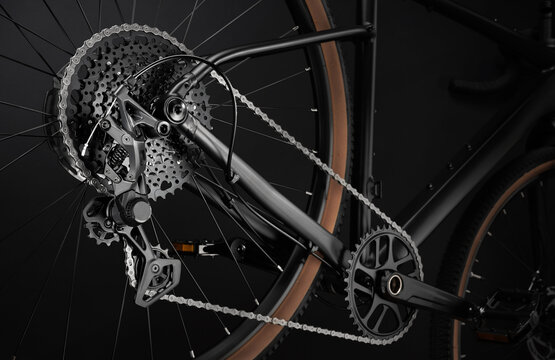 Detailed close-up of a modern gravel bicycle drivetrain. Multi-speed cassette, rear derailleur, chain and crankset against dark background.