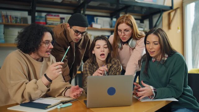 Group of students studying together in a library while looking at a laptop and discussing their work in the afternoon